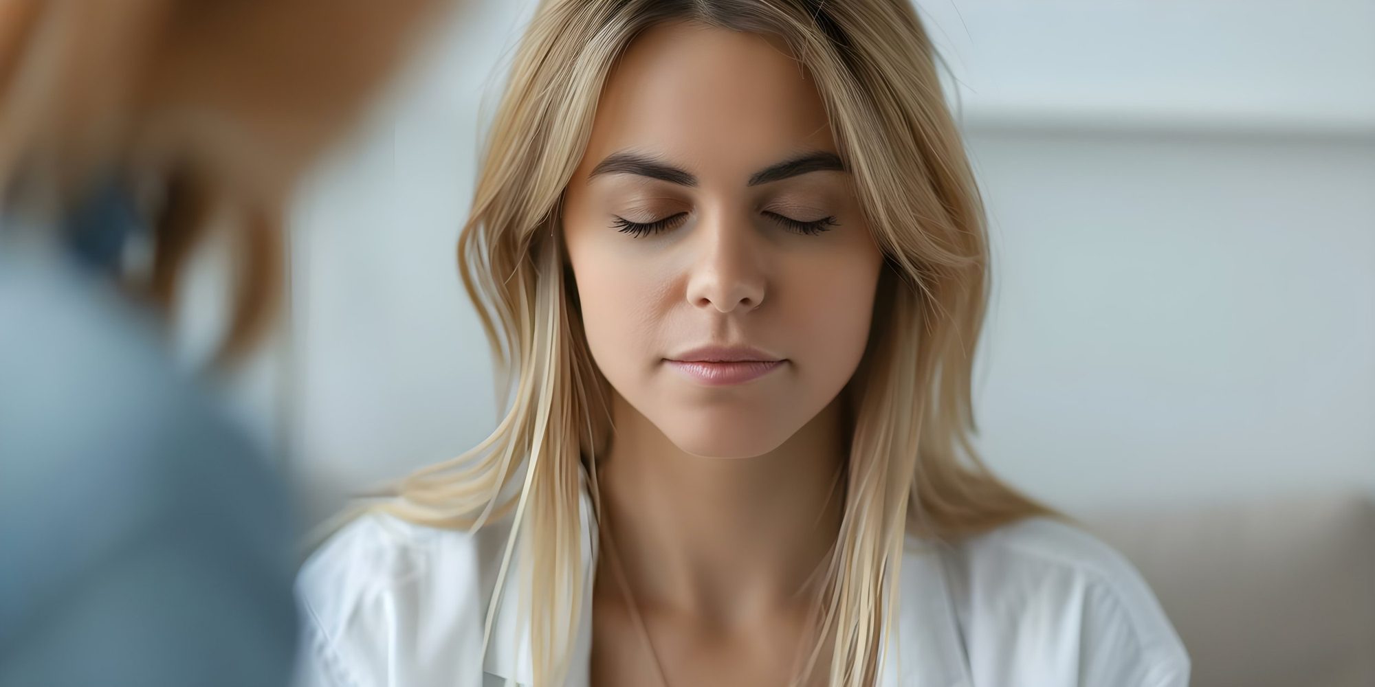 Close-up of a young woman with blonde hair and closed eyes, appearing calm or meditative.