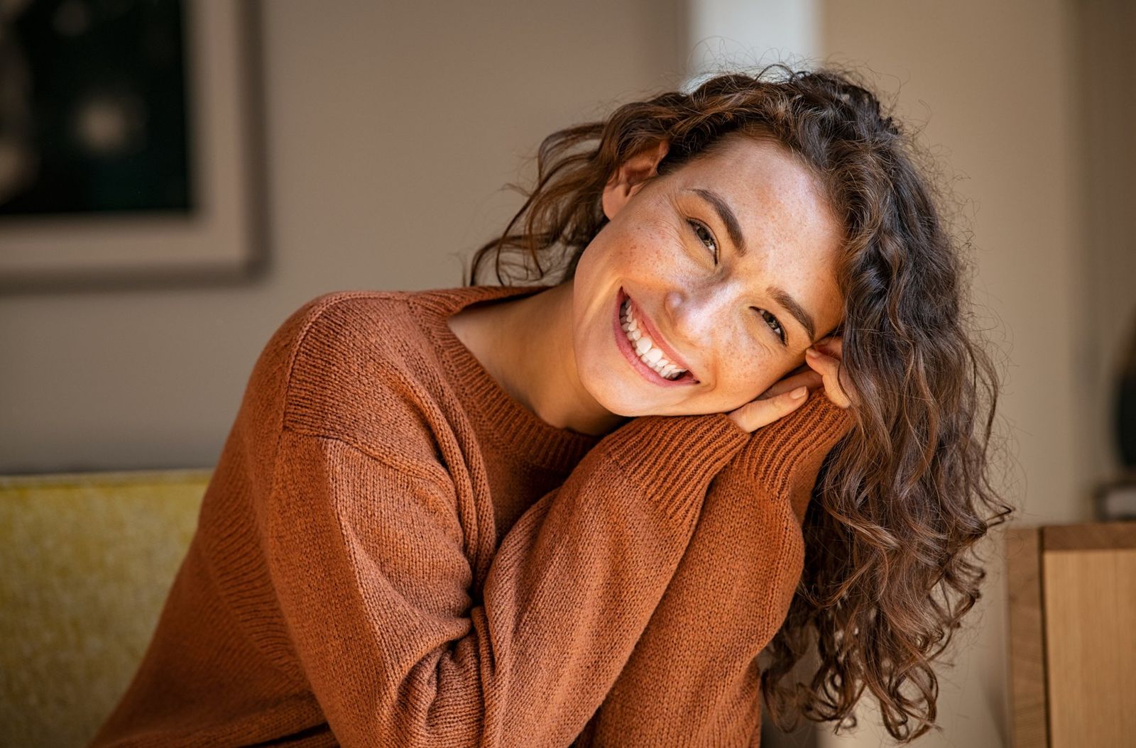 A woman with brown hair and an orange shirt smiles as she looks ahead
